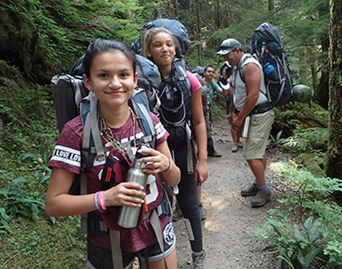 Young girls hiking on a mountain trail with others pausing for a break to drink water